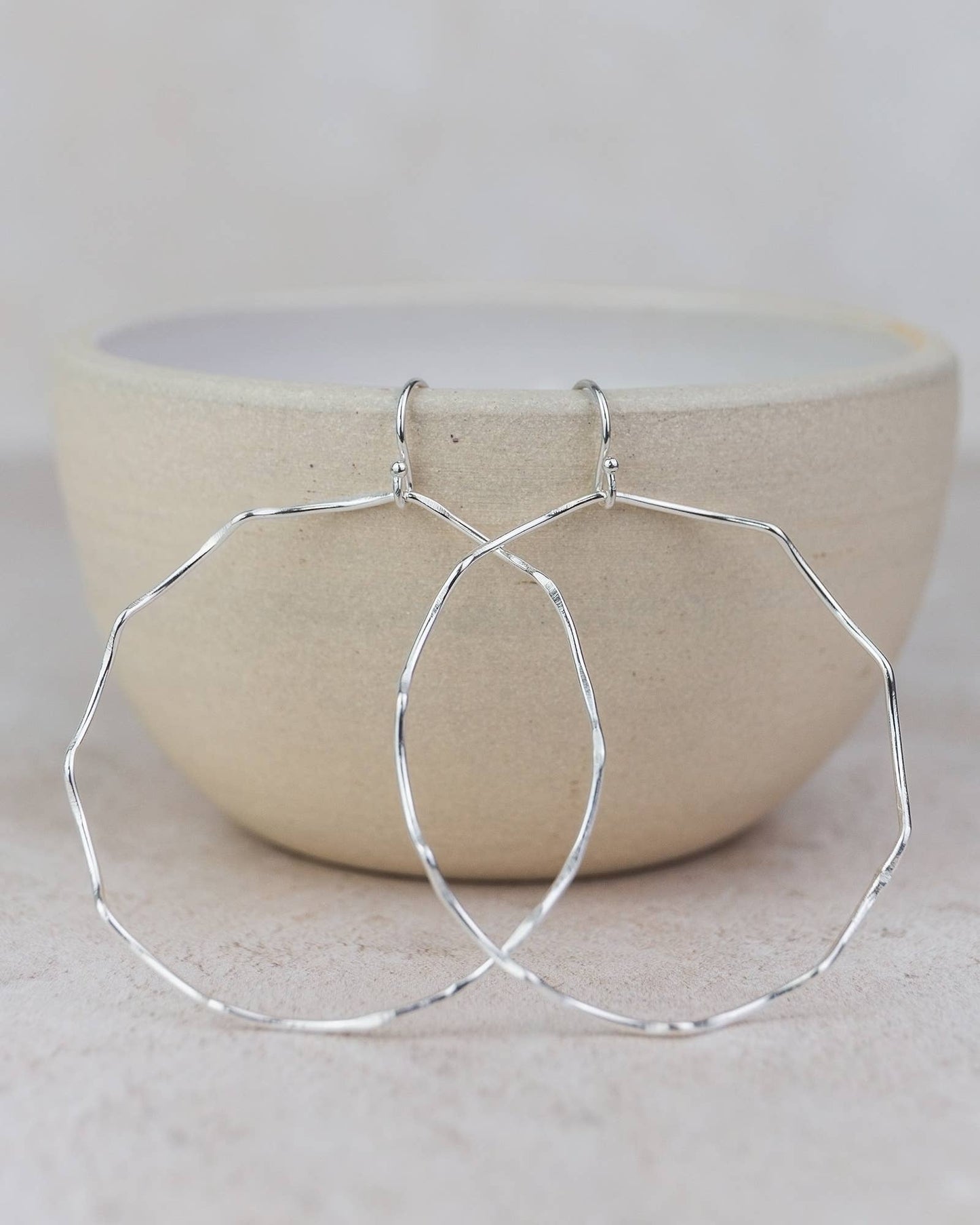 Silver hoop earrings on a light gray surface with a beige bowl in the background